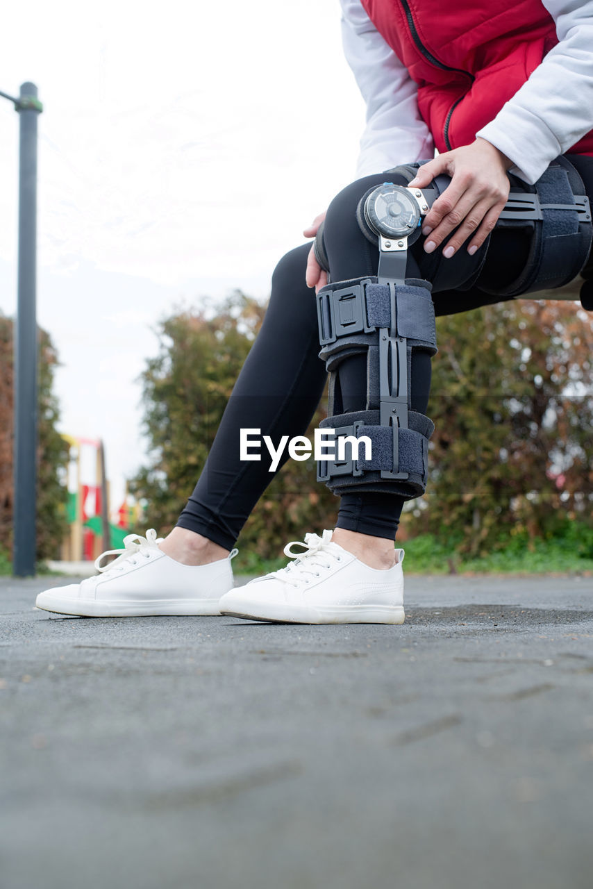 Woman wearing sport clothes and knee brace or orthosis after leg surgery, walking in the park