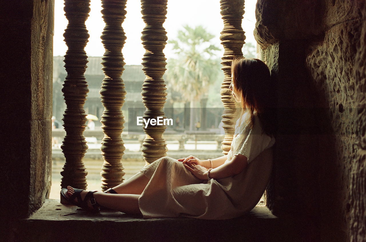 Side view of thoughtful woman sitting on window sill