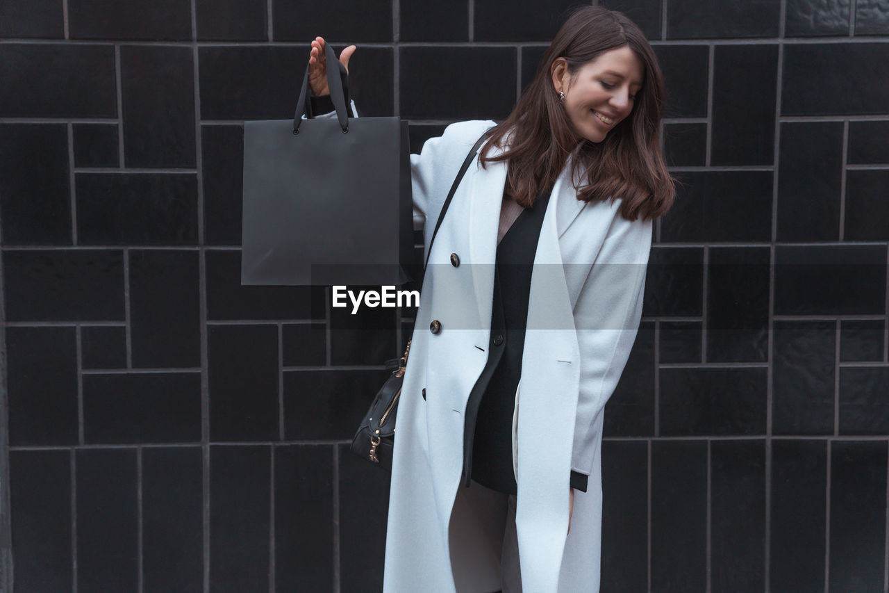 Smiling woman holding bag against wall outdoors