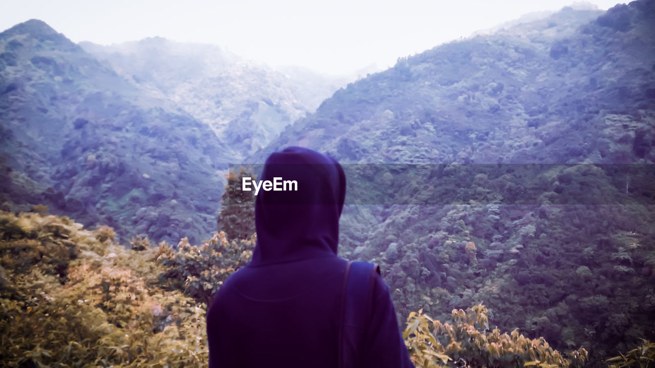 REAR VIEW OF MAN LOOKING AT MOUNTAIN RANGE