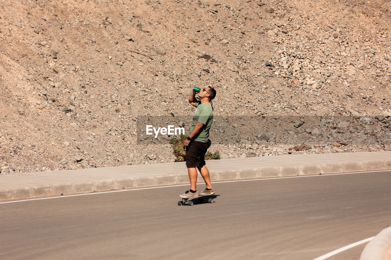 A man playing figure skating on a rural road in the sun on a bright day, play surf skate