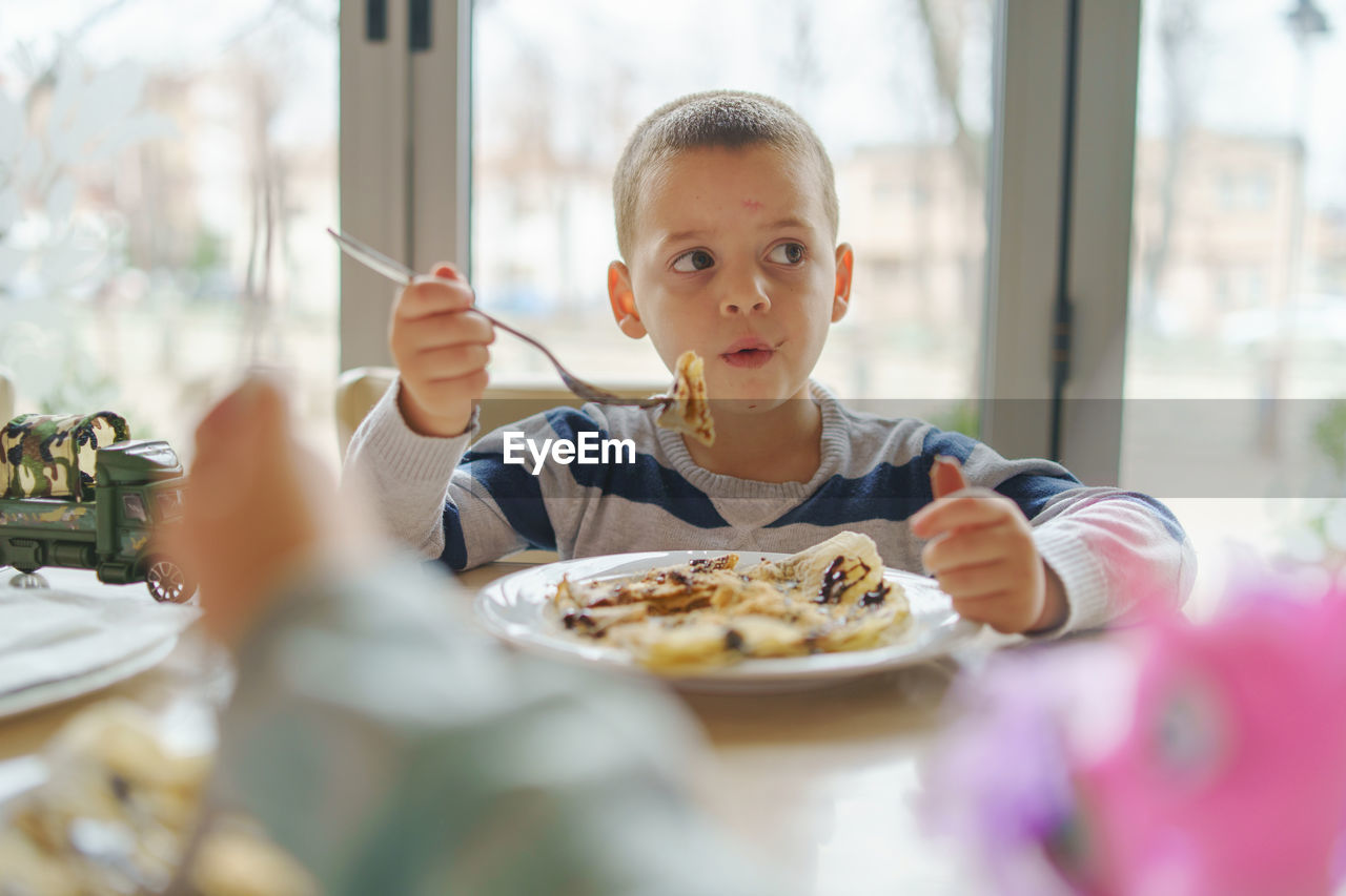 Boy eating food while sitting at table in restaurant