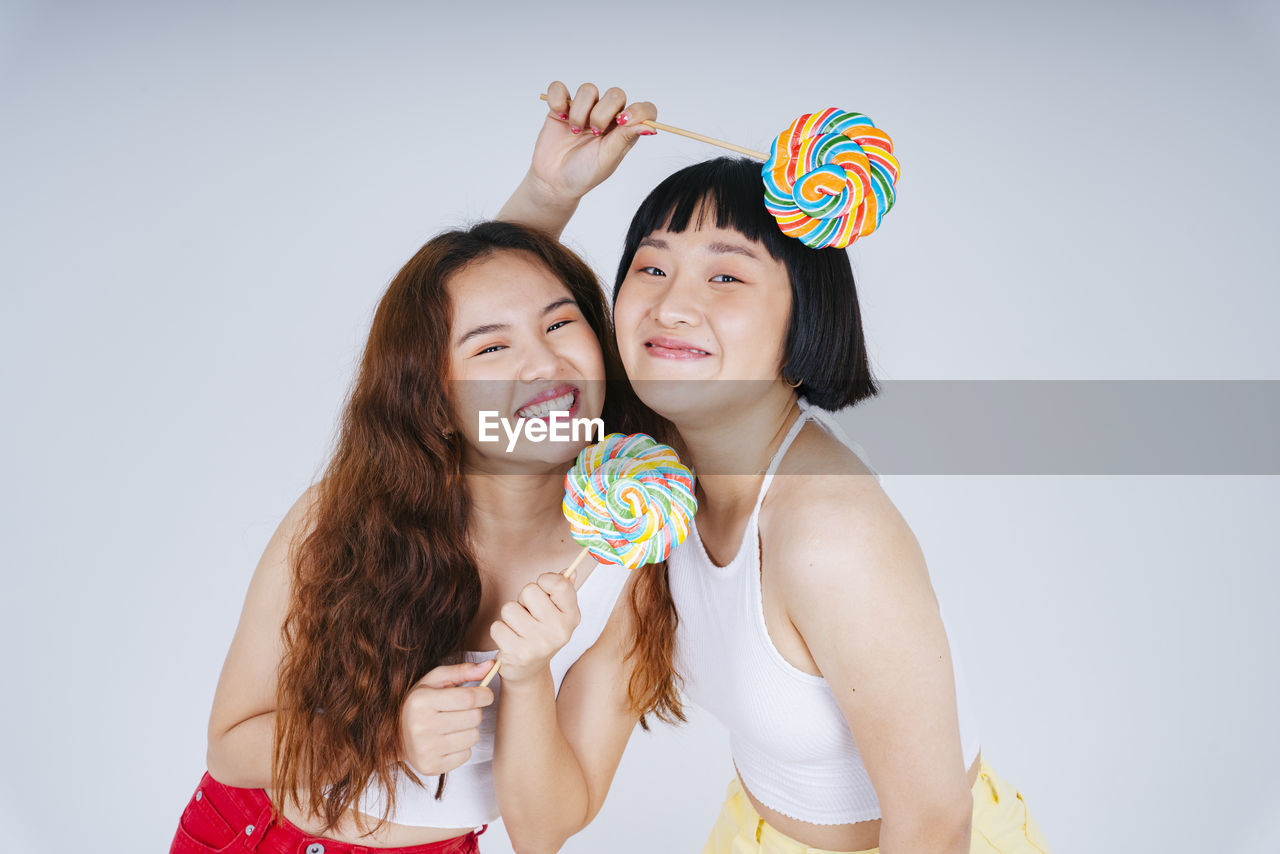 Portrait of lesbian couple holding lollipop against white background