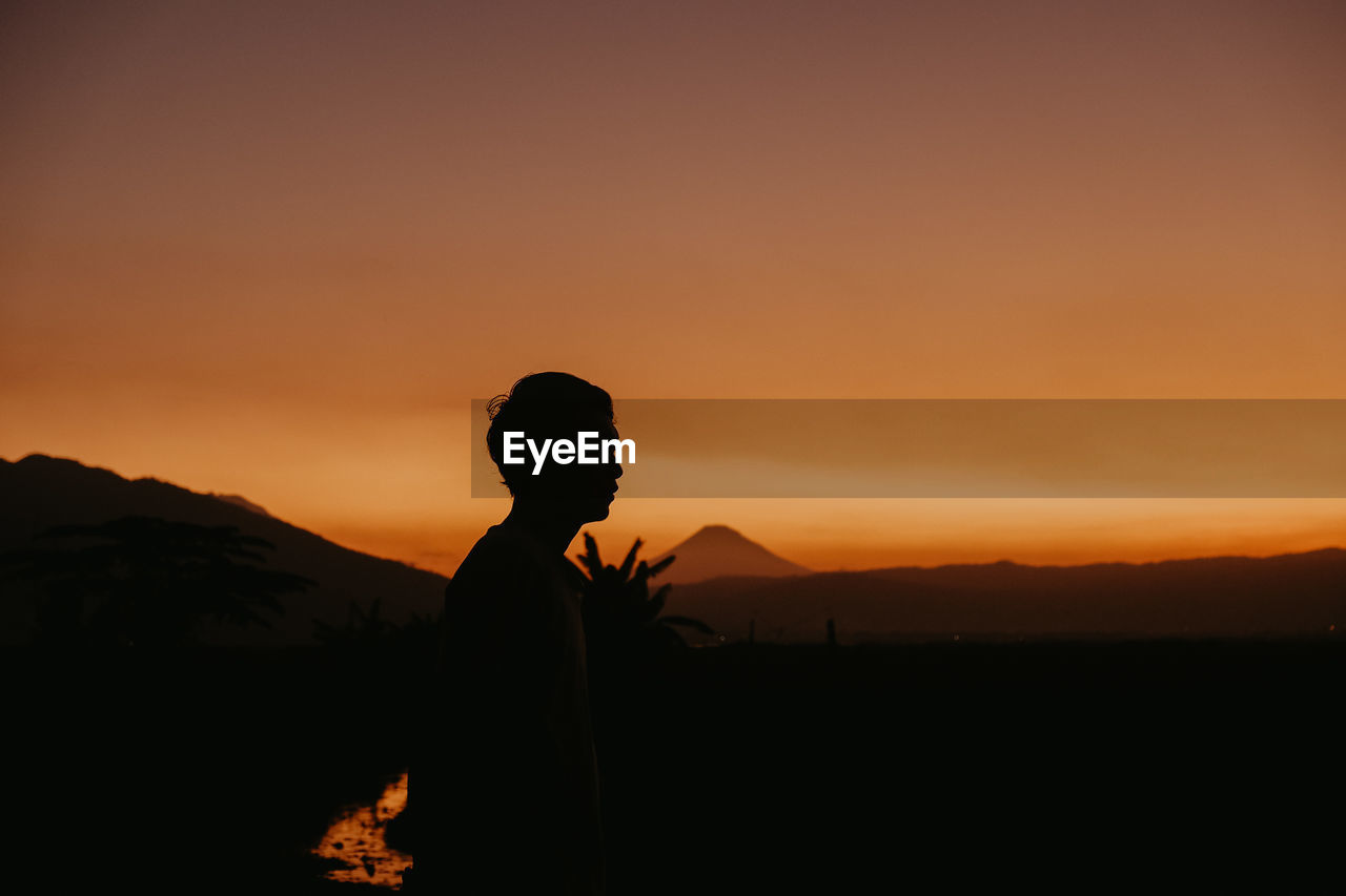 Silhouette person standing on land against sky during sunset