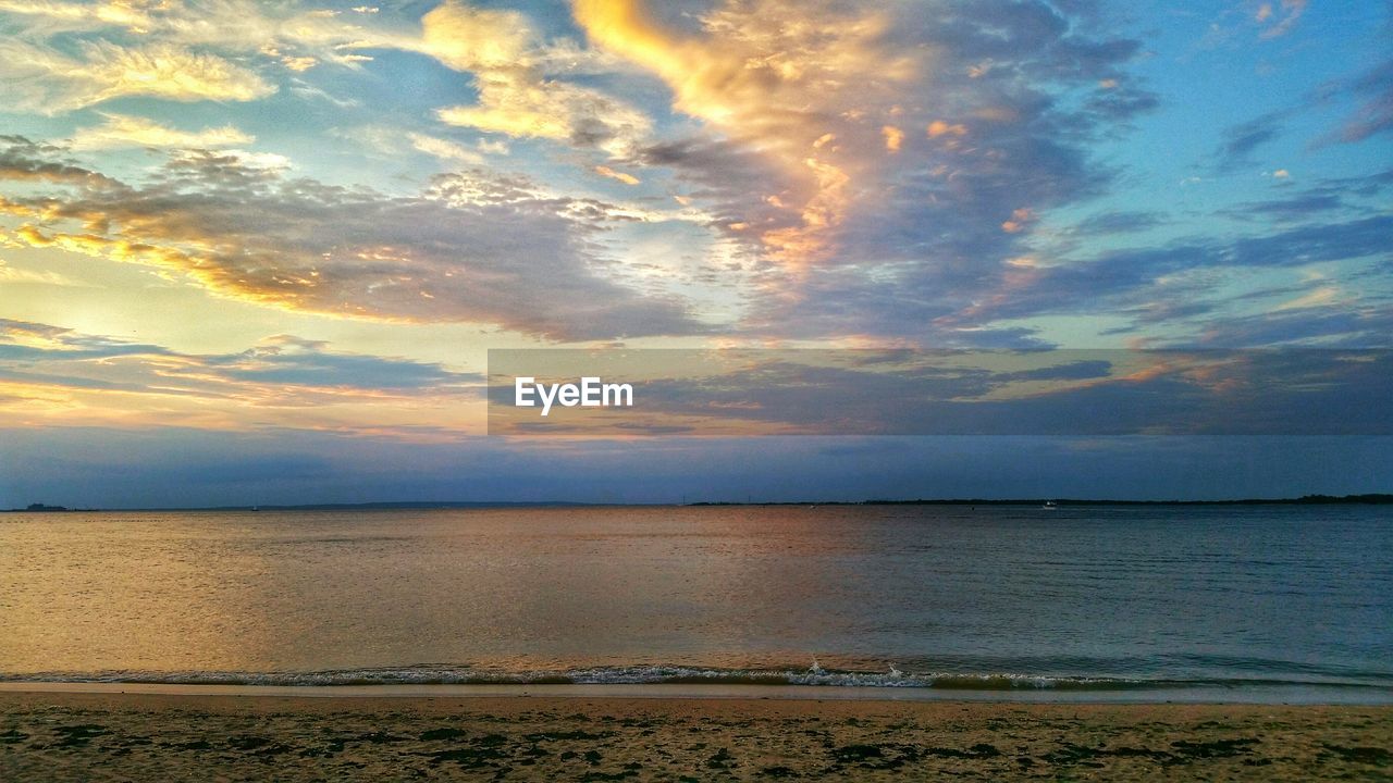 Scenic view of beach against cloudy sky during sunset