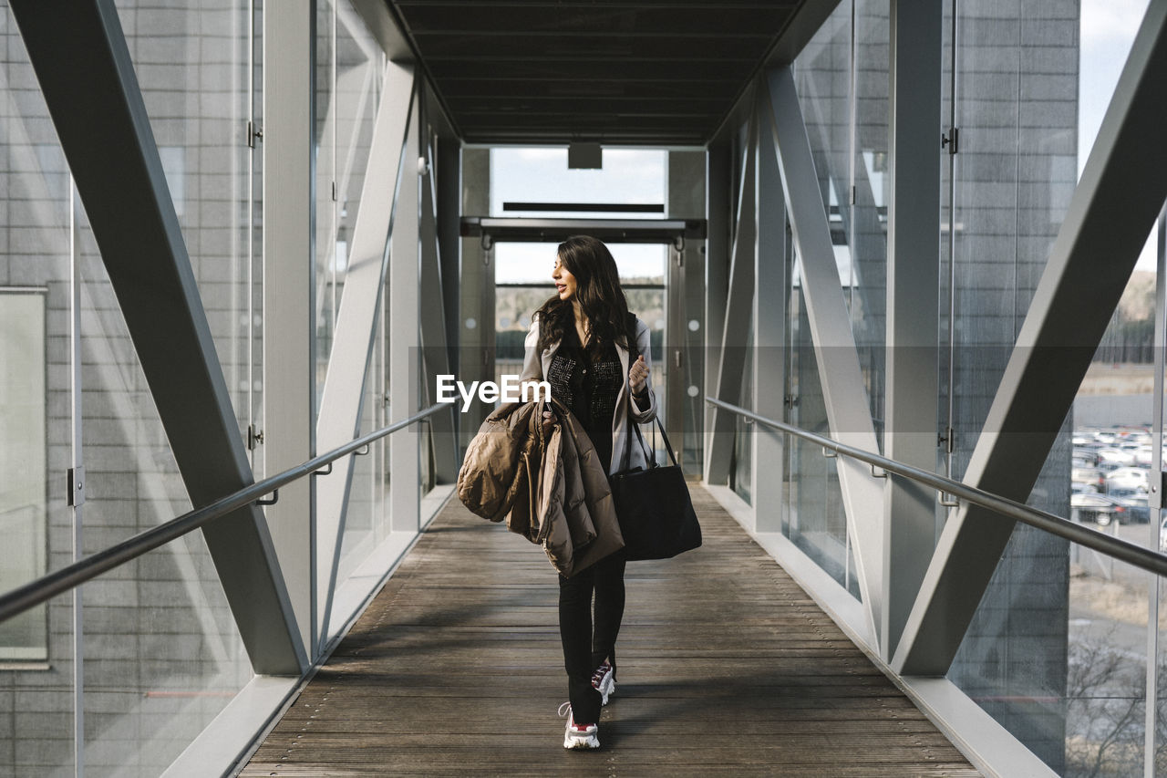 Businesswoman looking away holding bag while walking on footbridge