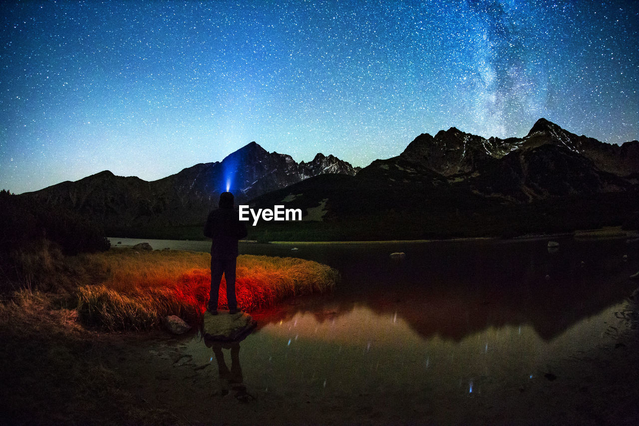 Silhouette man standing by lake against sky at night