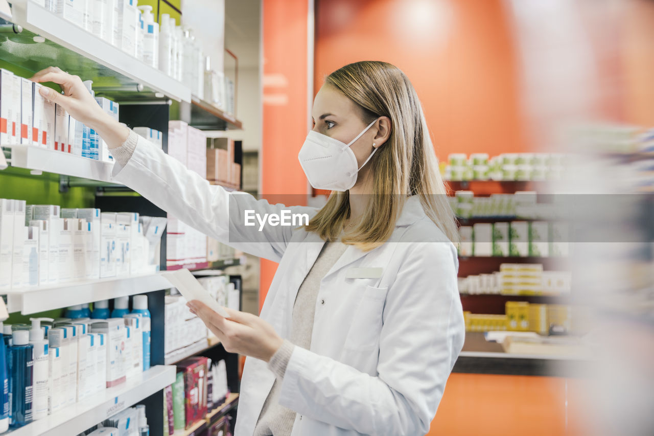 Female pharmacist wearing protective face mask while working in chemist shop