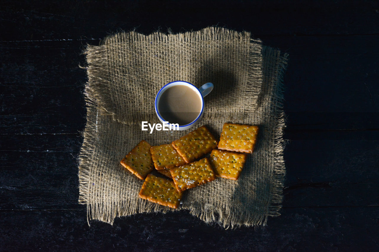 A cup of tea with biscuits on old wooden dark background