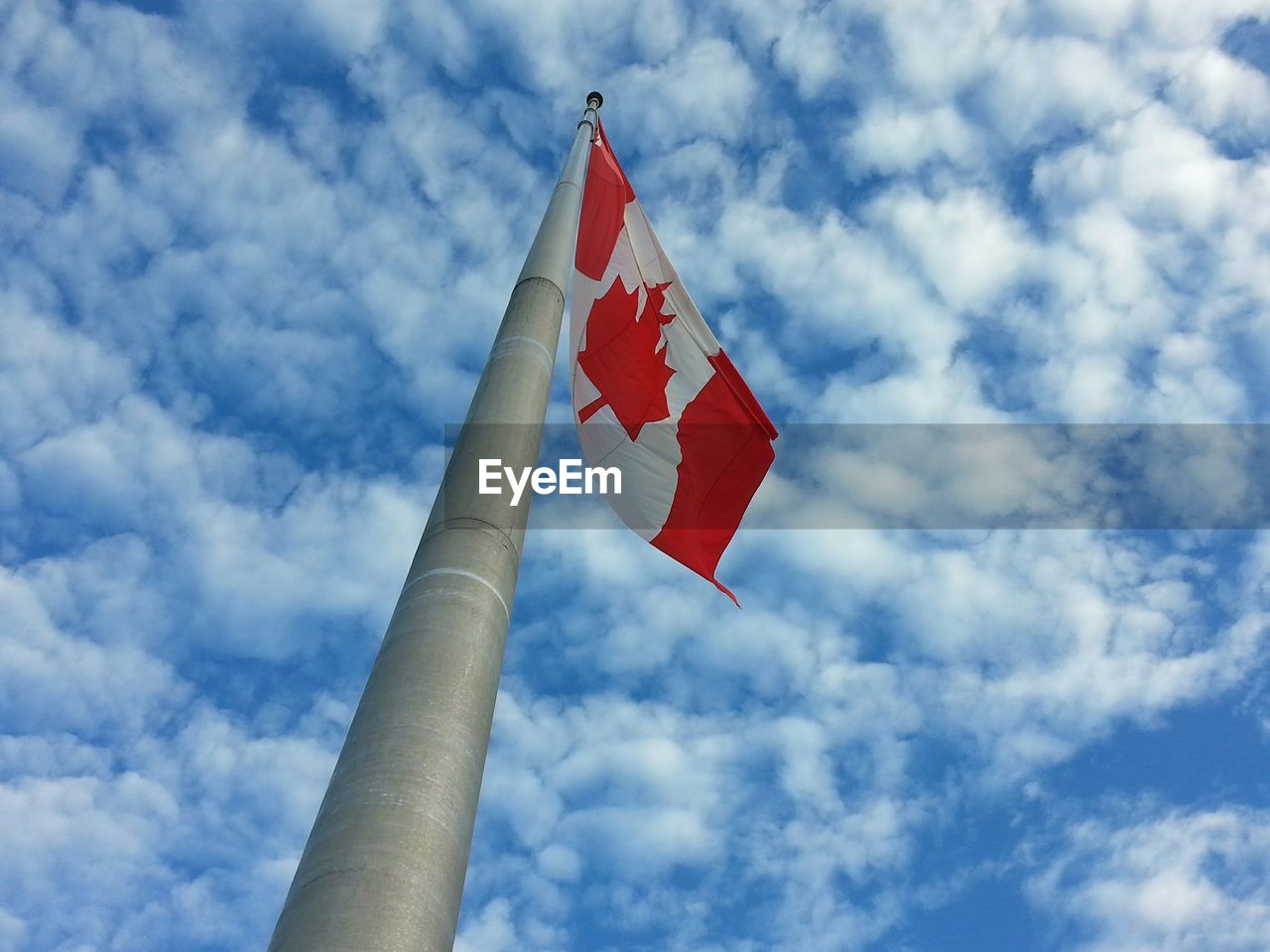 Low angle view of canadian flag against blue cloudy sky