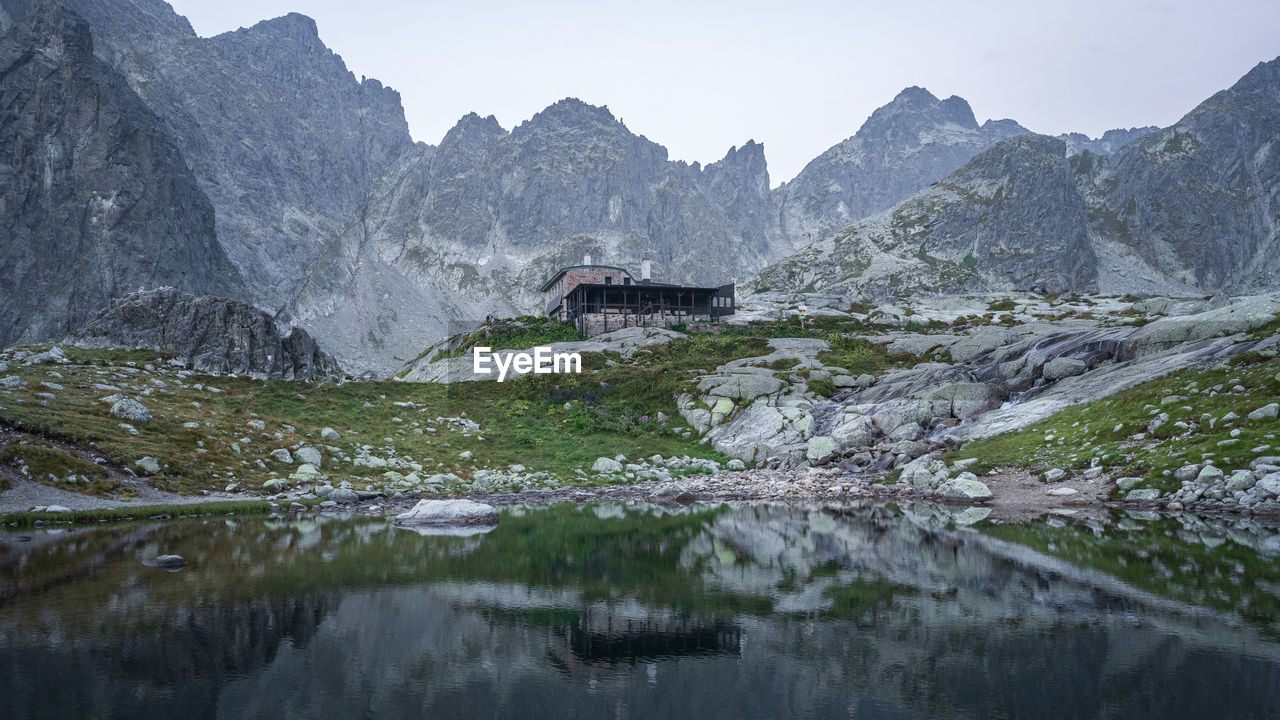 Alpine cabin surrounded by sharp peaks reflected in foreground tarn during dawn, slovakia, europe
