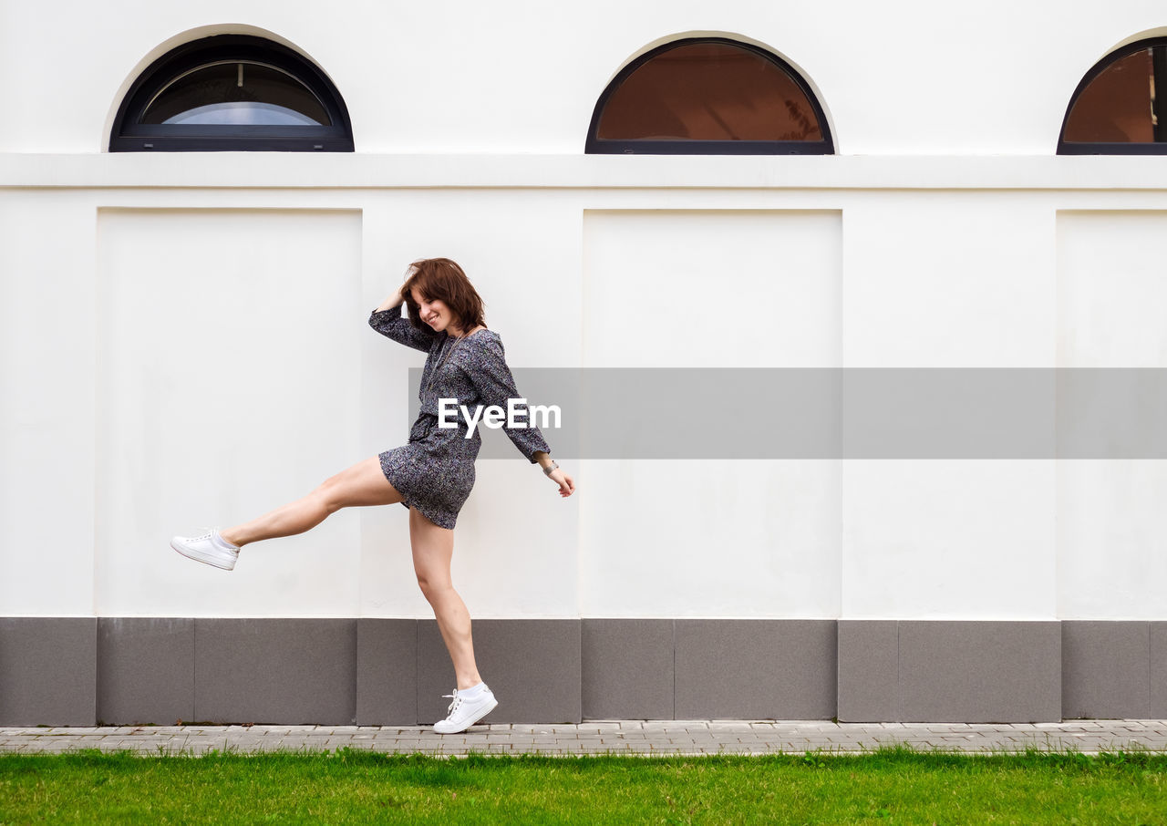 Happy young woman in short dress walks along the building