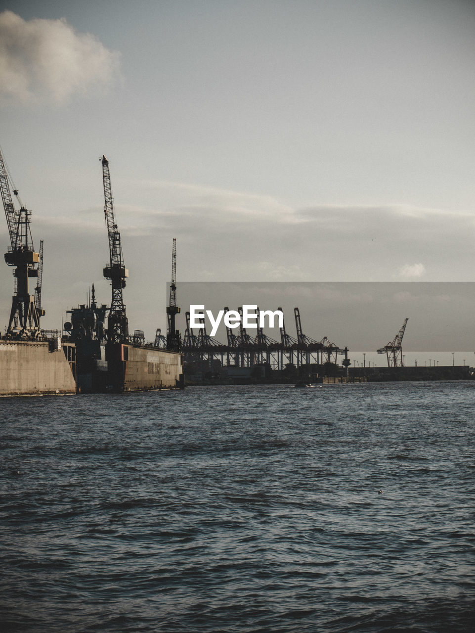 Cranes at commercial dock against sky