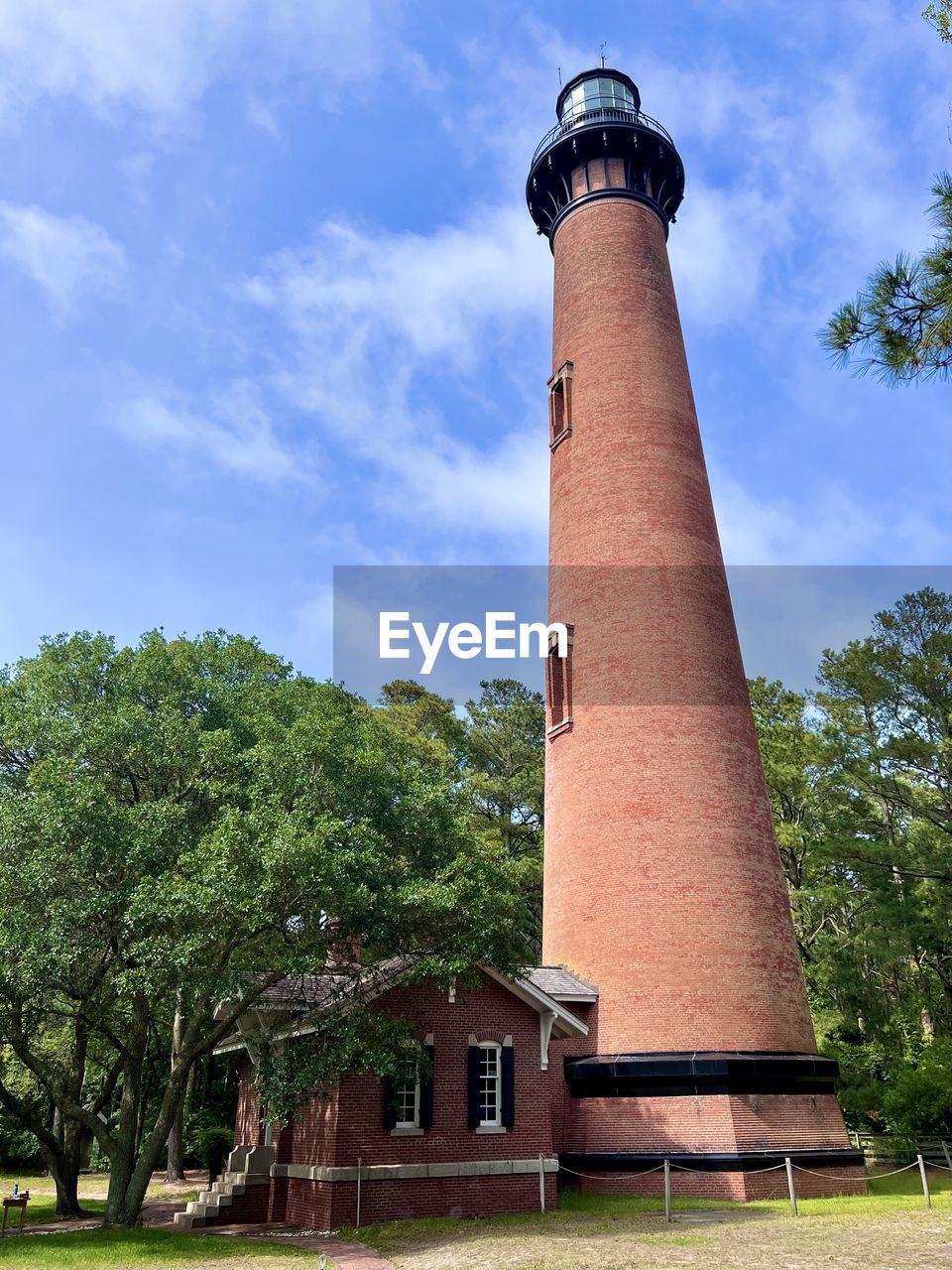 architecture, lighthouse, built structure, building exterior, tower, plant, guidance, tree, sky, building, nature, protection, security, cloud, no people, history, day, the past, house, outdoors, observation tower, travel destinations, blue, low angle view, grass, travel, environment