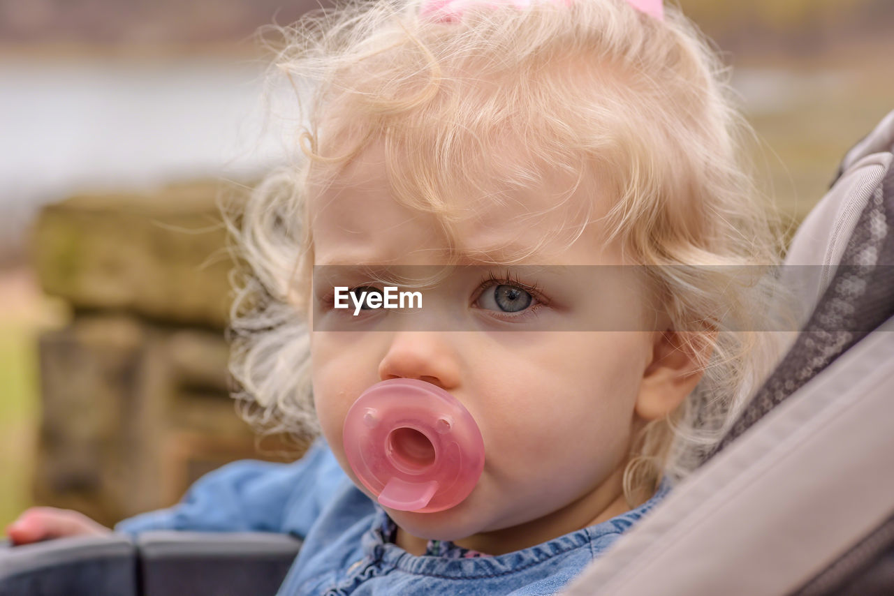 Close-up of baby girl with pacifier in stroller