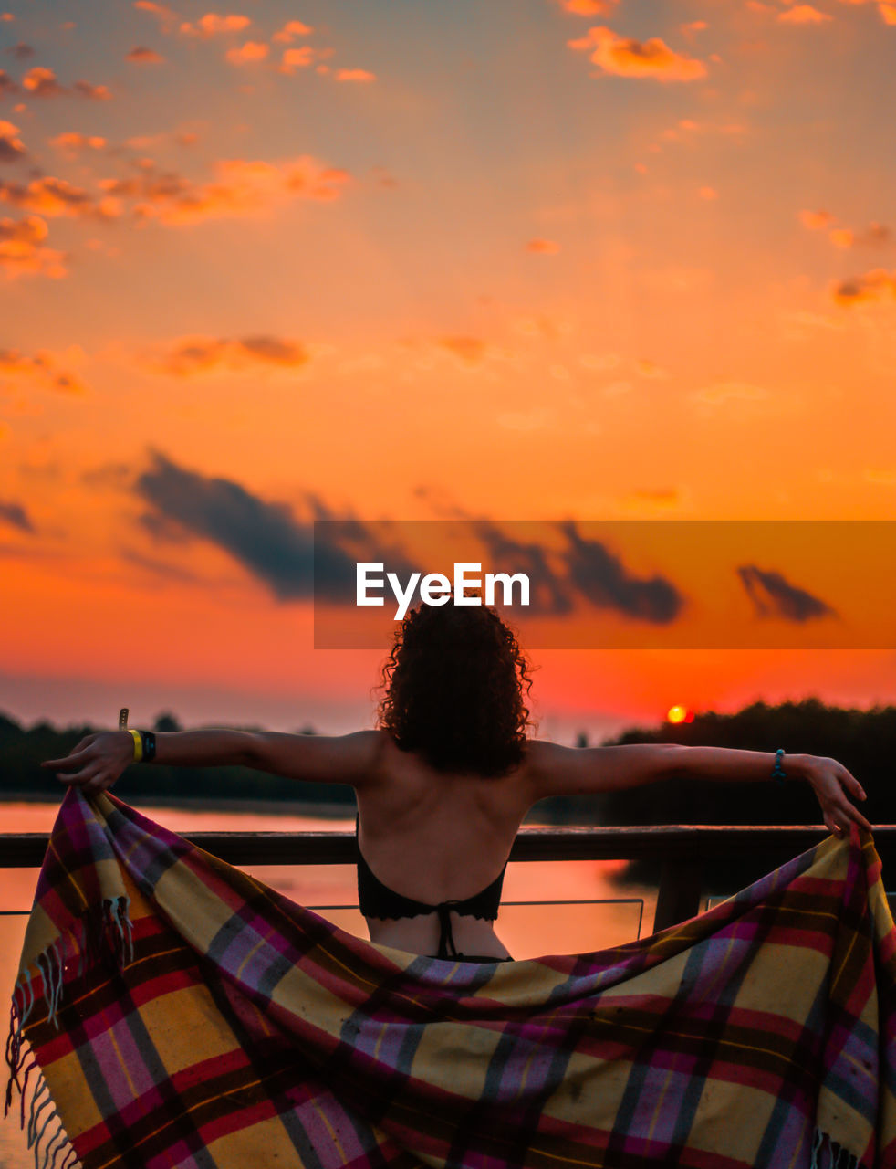 Rear view of carefree woman holding blanket while looking at sunset