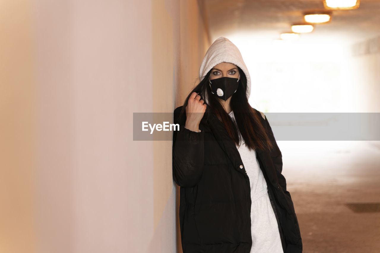 Mid adult woman wearing face mask and jacket standing in underground