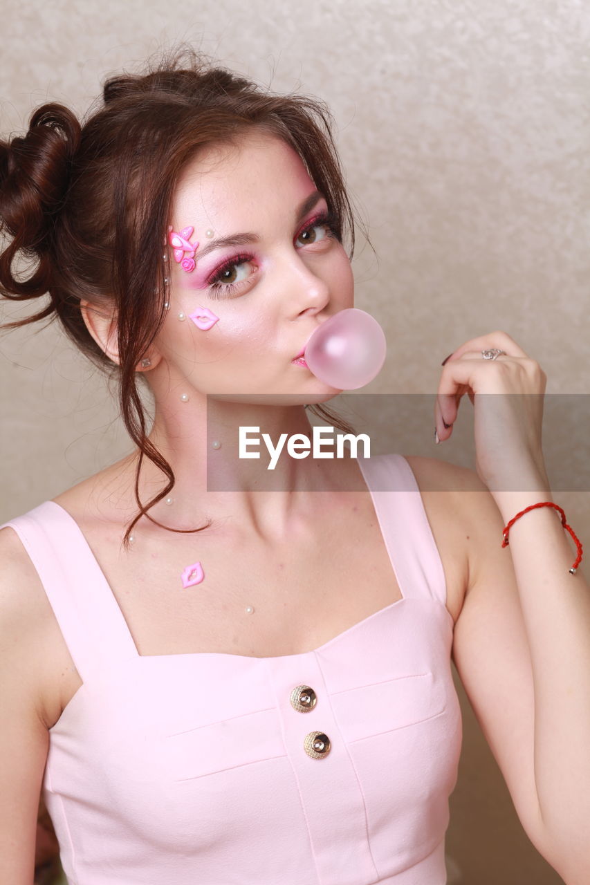 Young woman with pink make-up chewing gum against wall