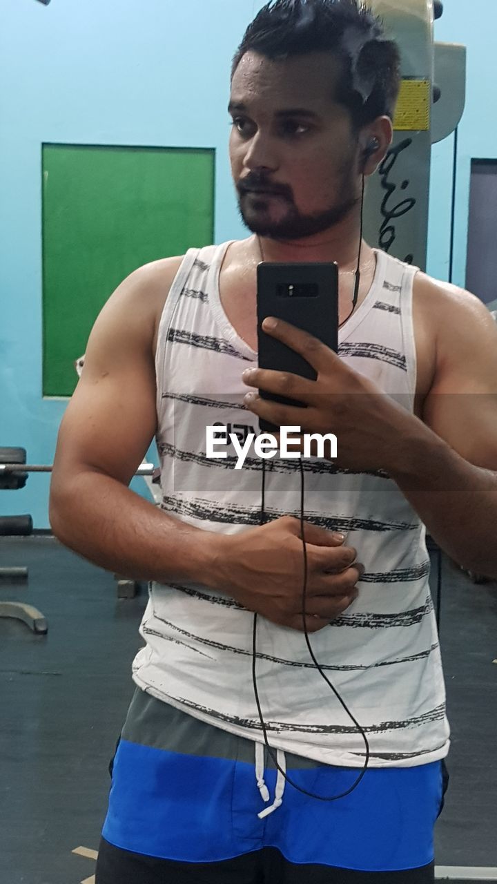 YOUNG MAN USING MOBILE PHONE WHILE STANDING ON CAMERA
