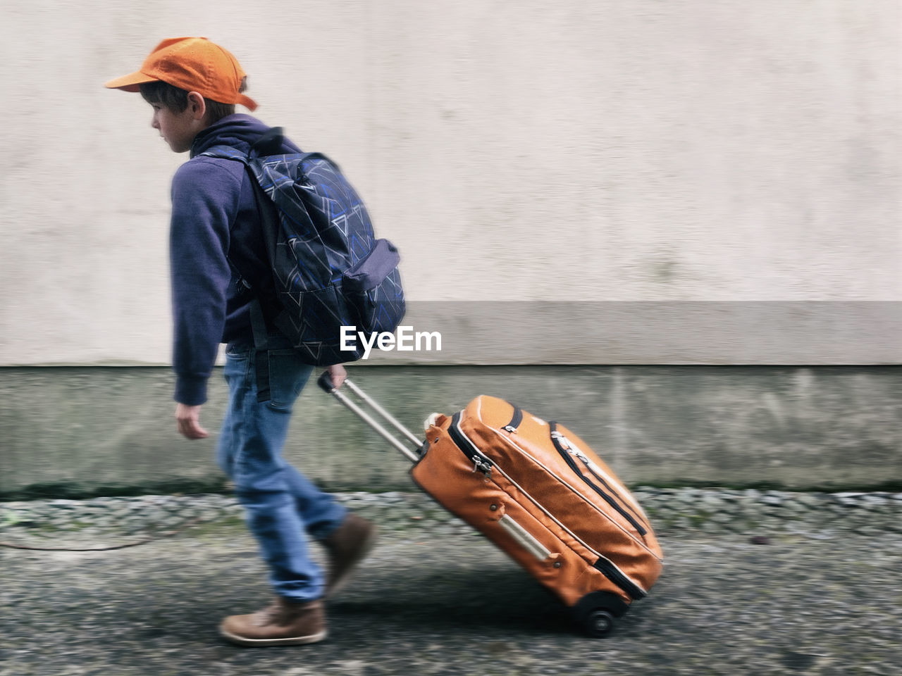 Side view of boy with luggage walking on footpath