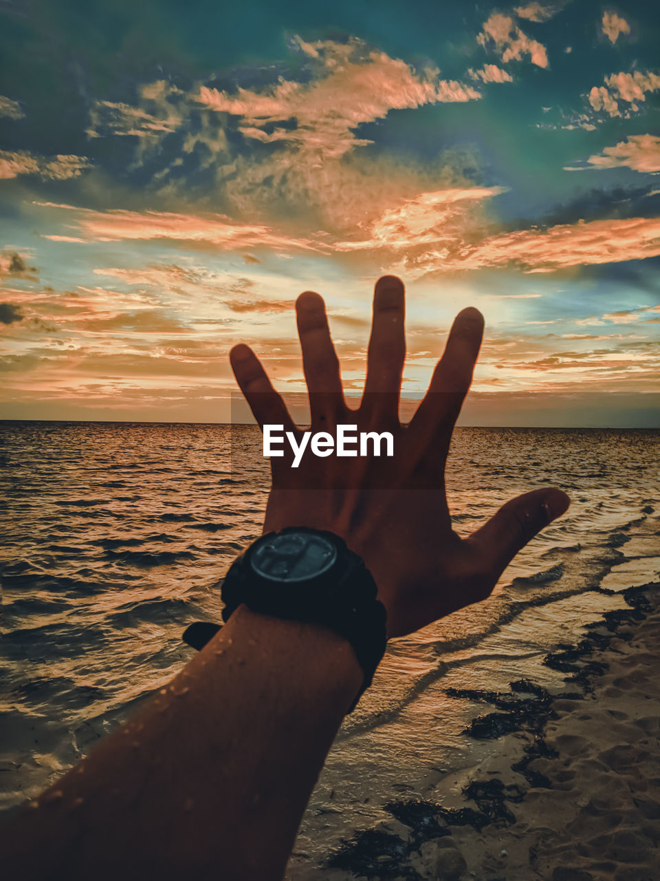 Midsection of person at sea shore against sky during sunset