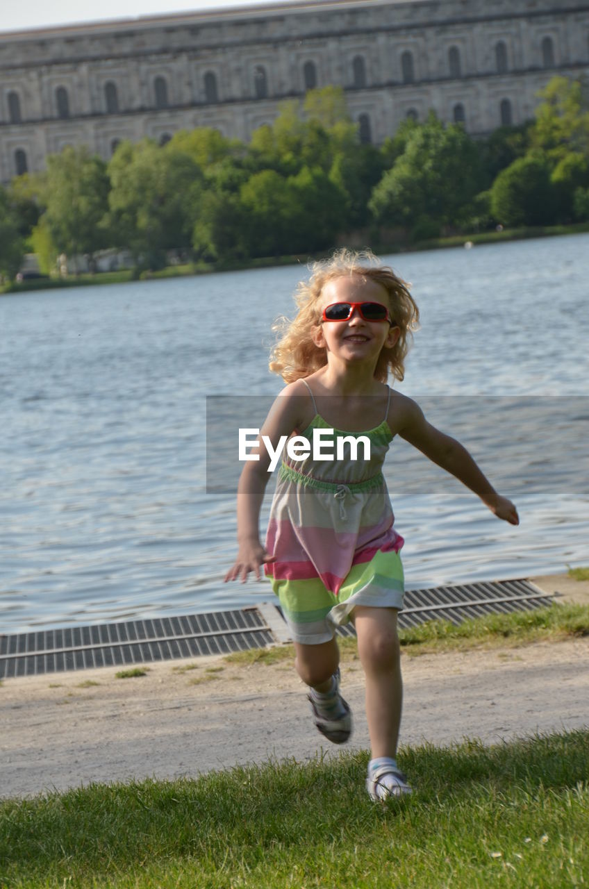 Full length of happy girl standing running on riverbank against building