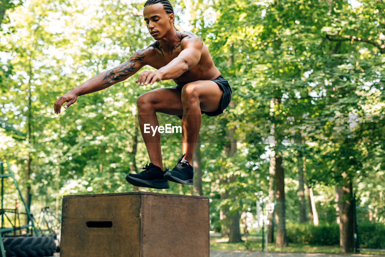 Shirtless male athlete jumping on box at park
