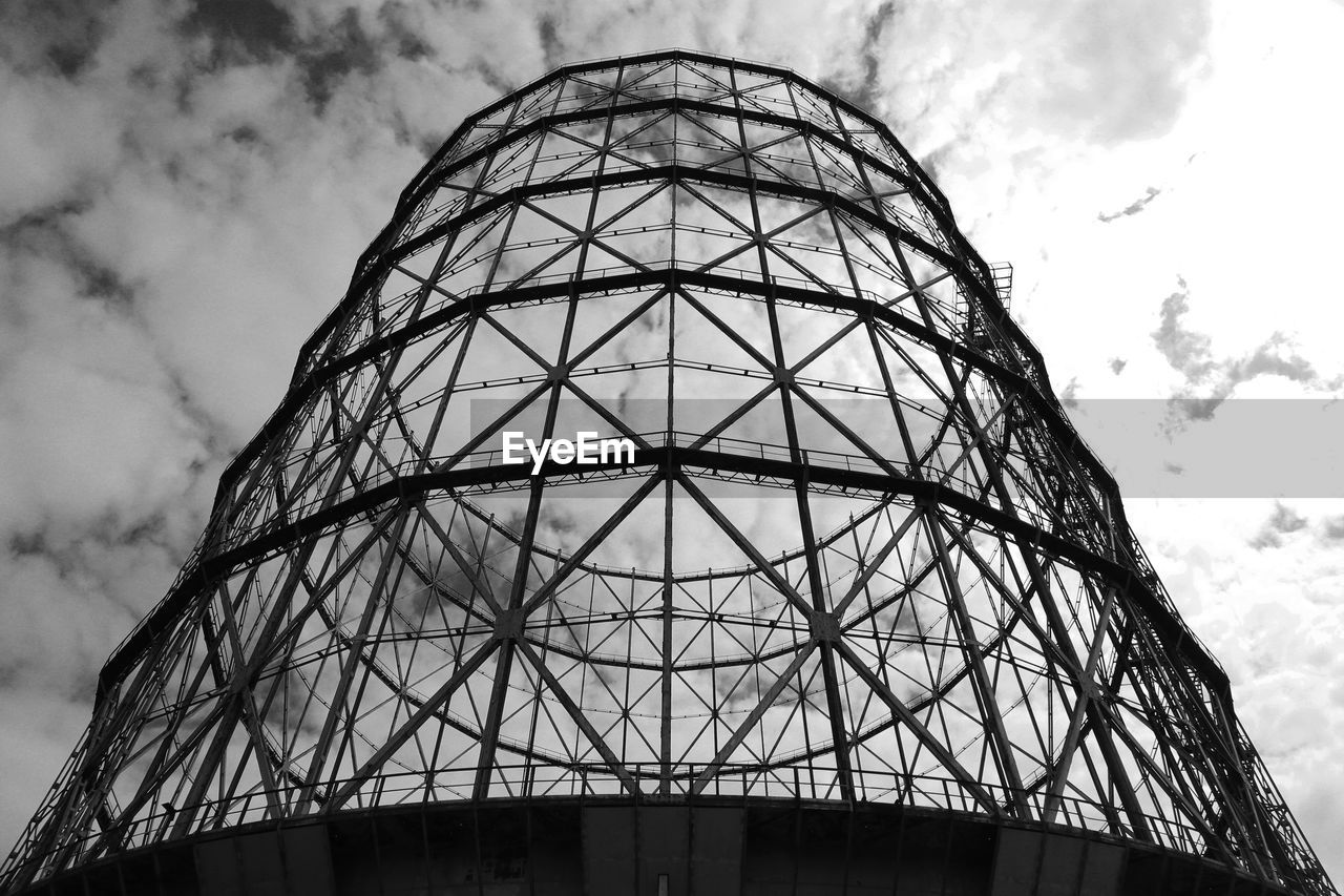 Low angle view of gasometer against cloudy sky