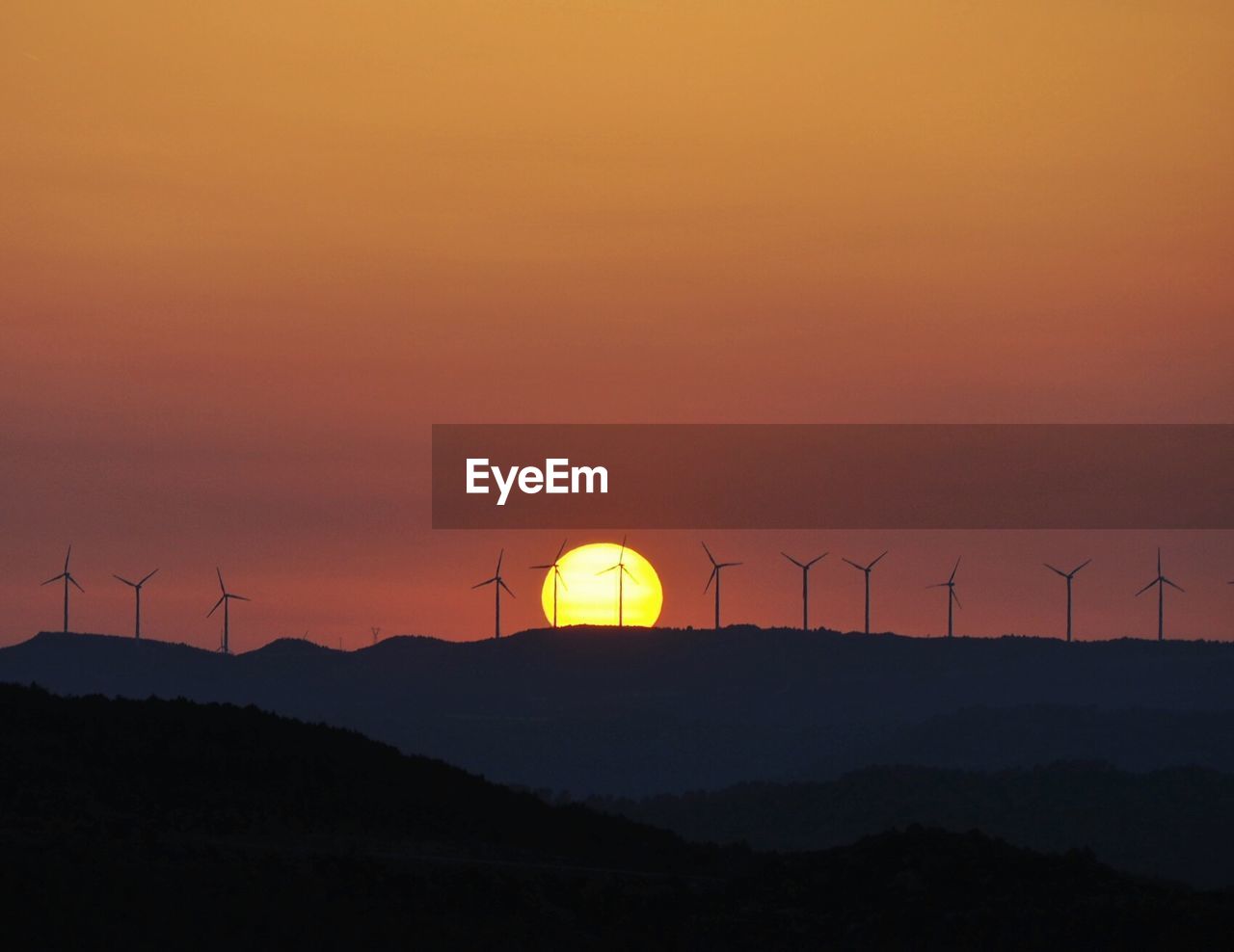Distance shot of wind turbines on landscape at sunset