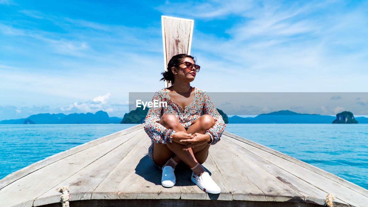 FULL LENGTH OF SMILING YOUNG WOMAN SITTING ON BEACH