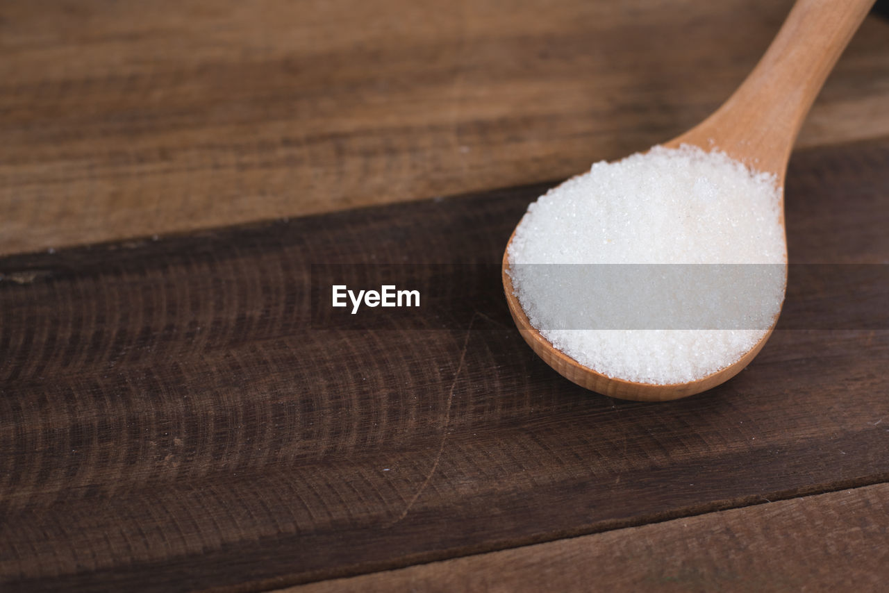 Heap of white sugar in a wooden ladle over wooden table. concept of unhealthy eating and diabetes