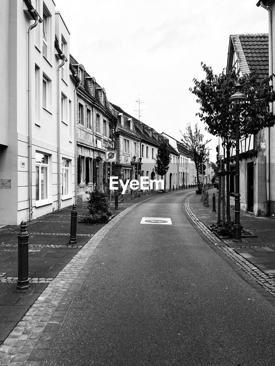 EMPTY ROAD ALONG BUILDINGS AND TREES