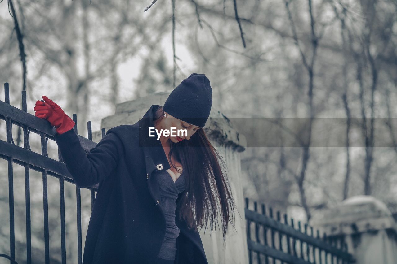 Woman standing against fence during winter