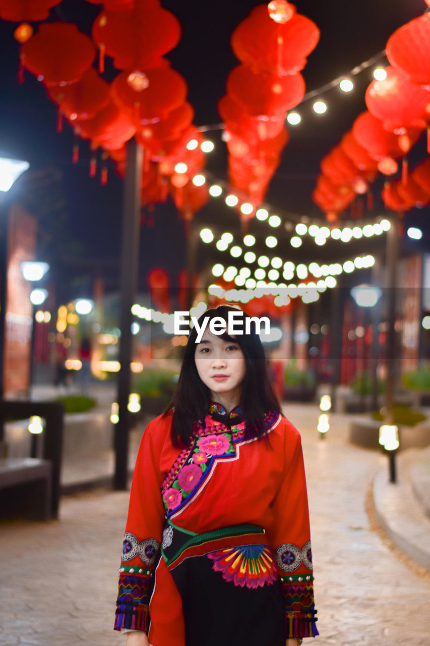 Portrait of woman standing against illuminated lights at night