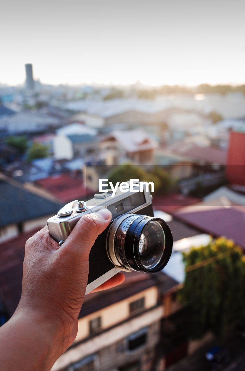 Close-up of hand holding camera against townscape