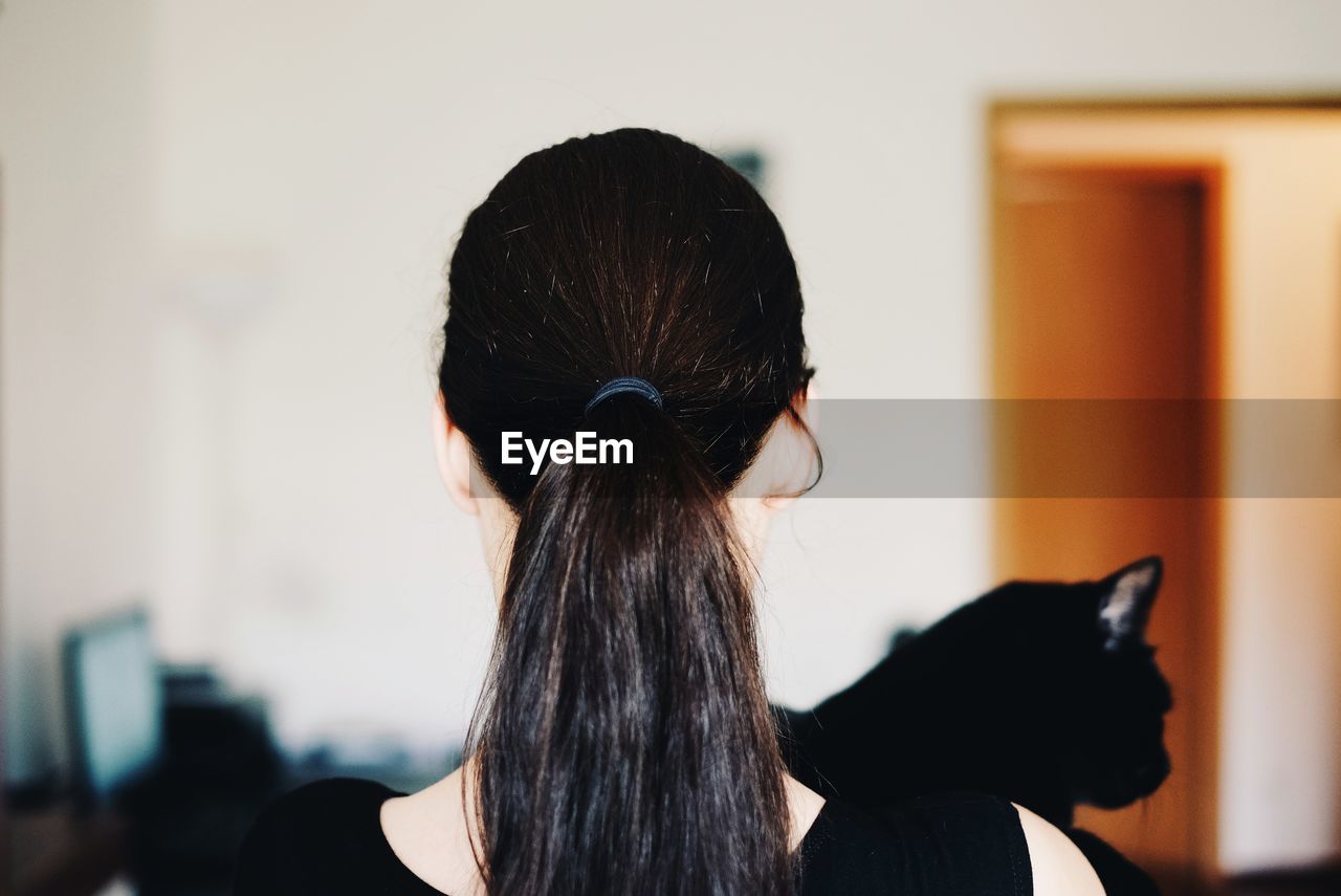 Rear view of woman with black cat at home