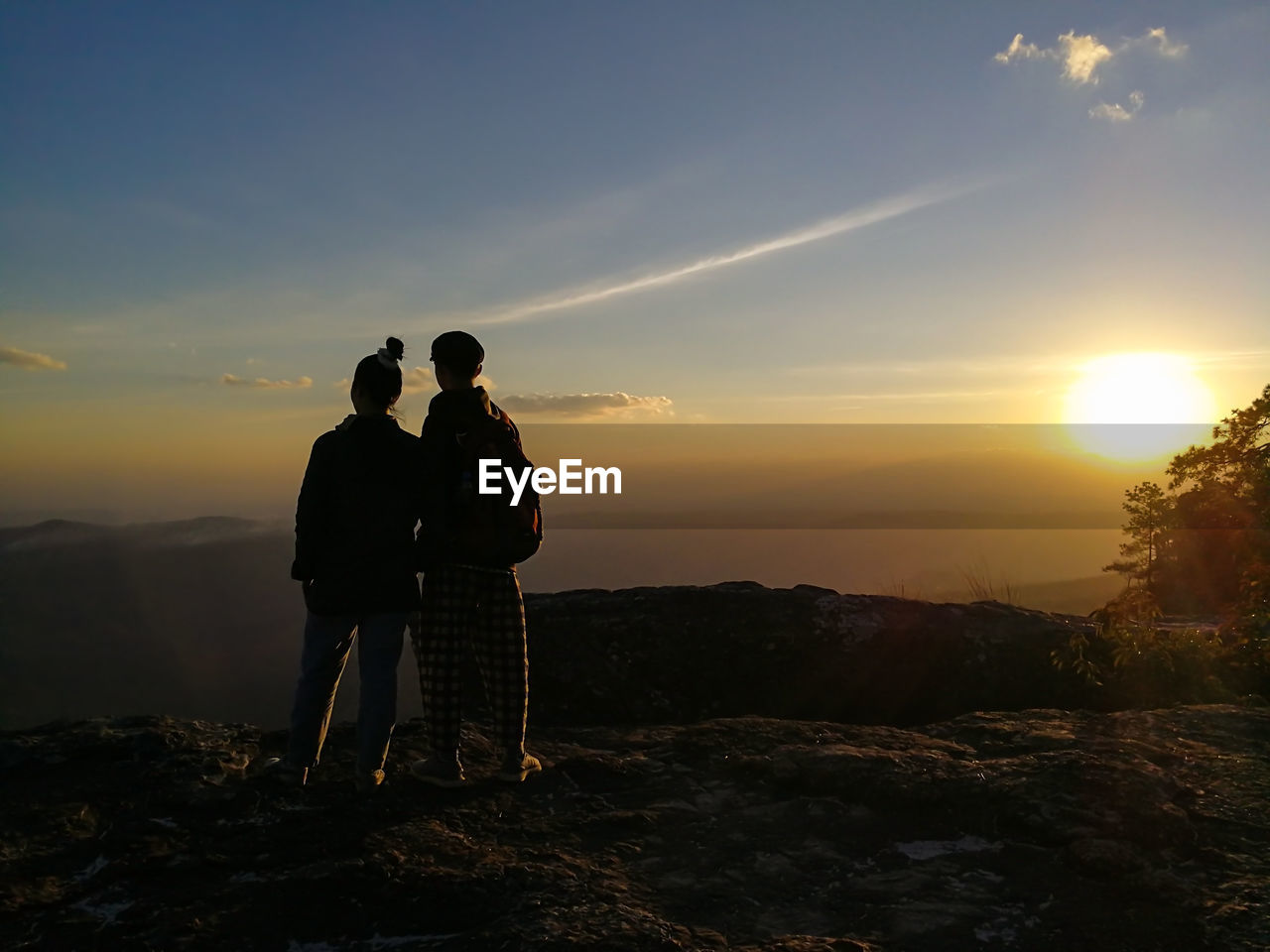 Rear view of couple standing against sky during sunset
