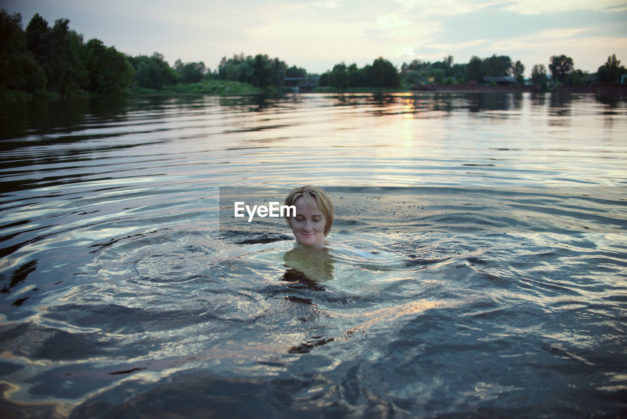 Woman swimming in lake at sunset