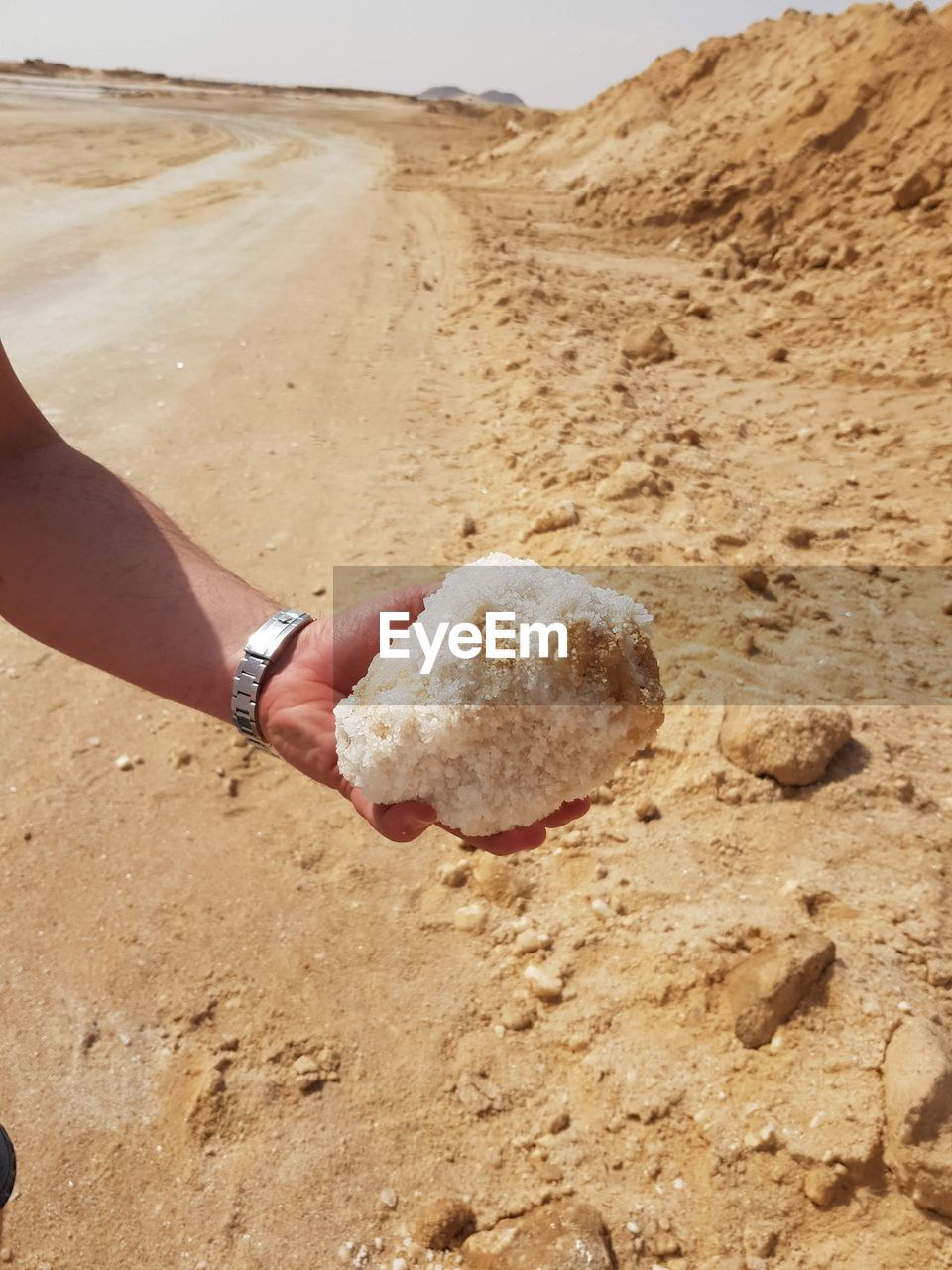 Cropped hand holding mineral at sandy beach