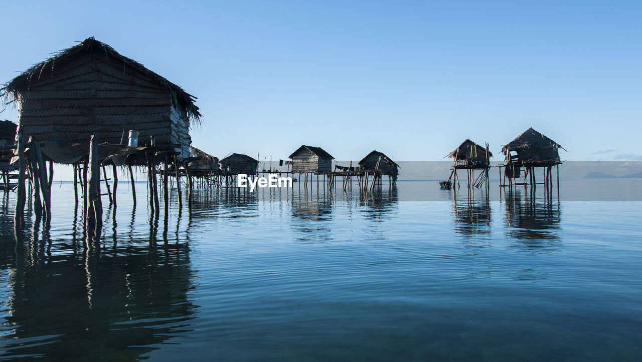 Stilt houses by sea against clear sky