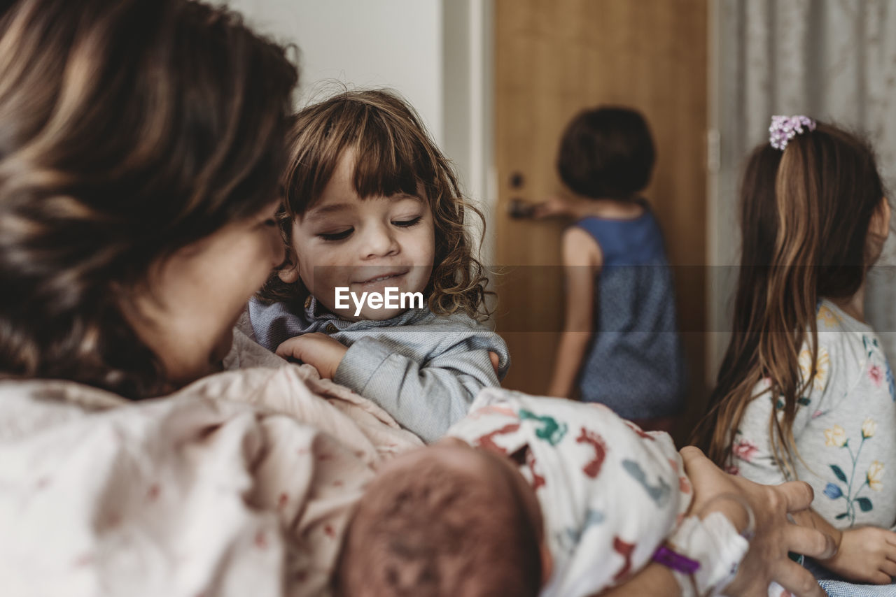 Side view of mother holding newborn son meeting siblings