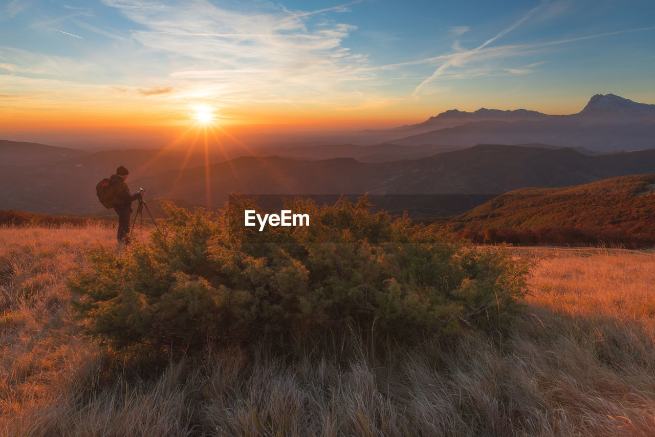 Man photographing on mountain against sky during sunset