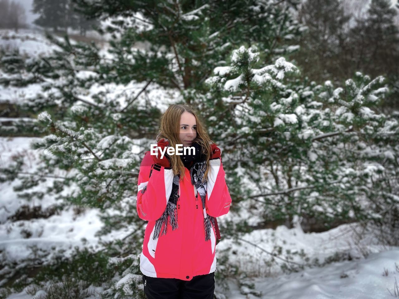 Young woman in winter clothes and pine trees covered in snow in the background