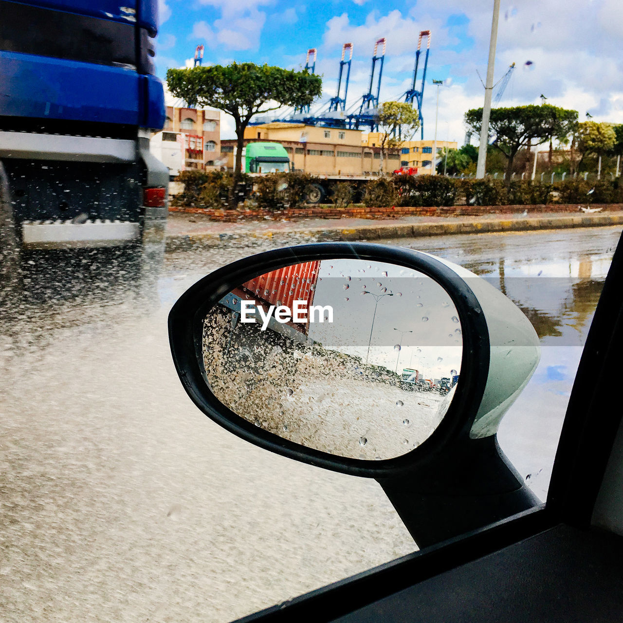 CLOSE-UP OF WET SIDE-VIEW MIRROR OF CAR ON ROAD