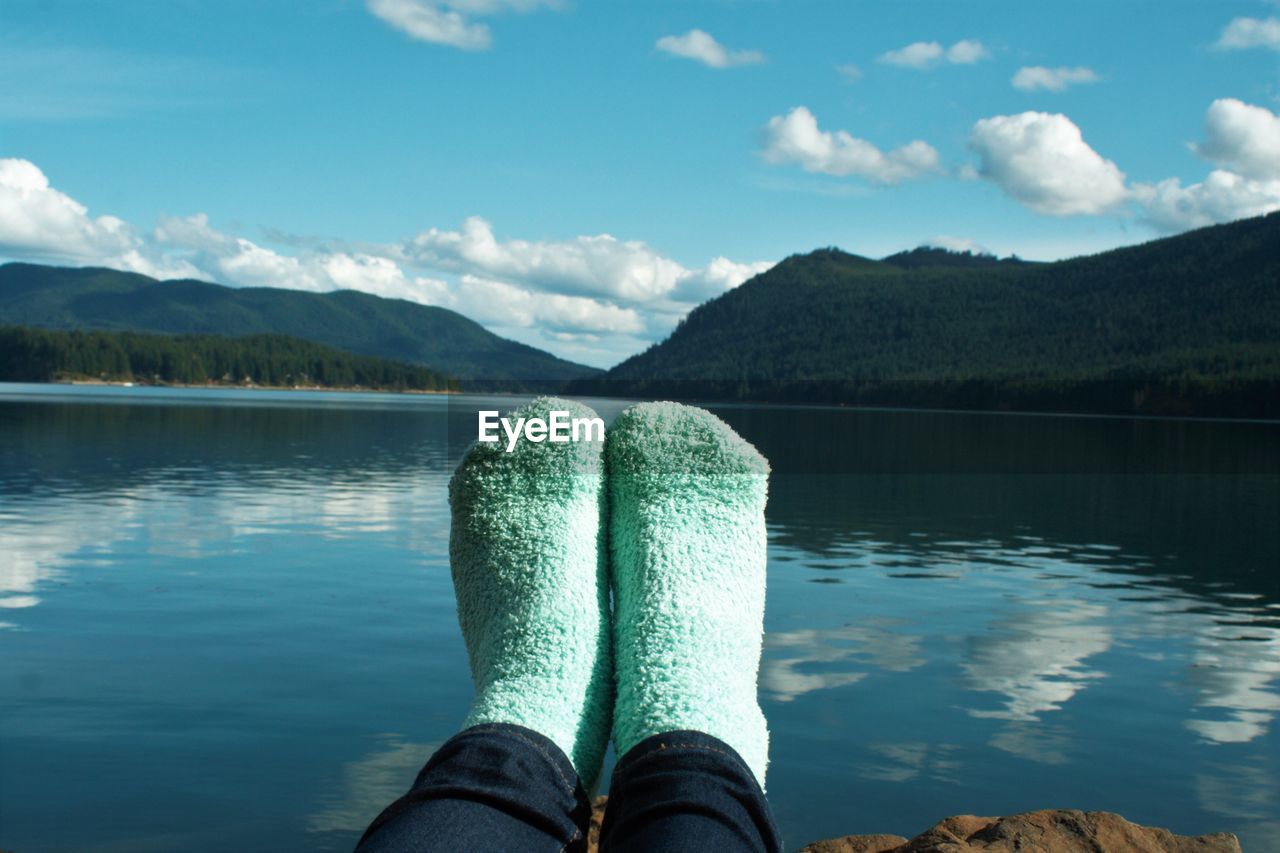 Low section of person wearing socks by lake against sky