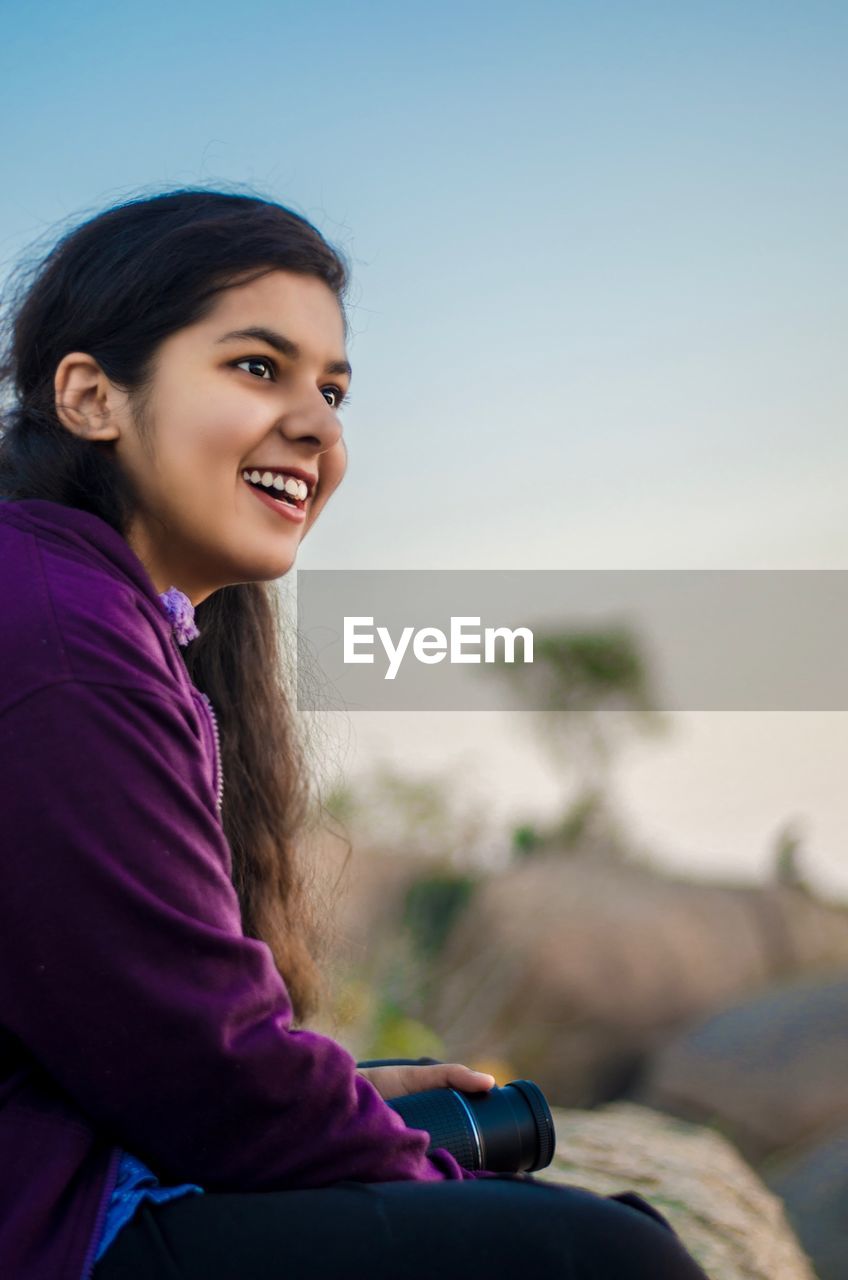 Side view of woman smiling while sitting against sky