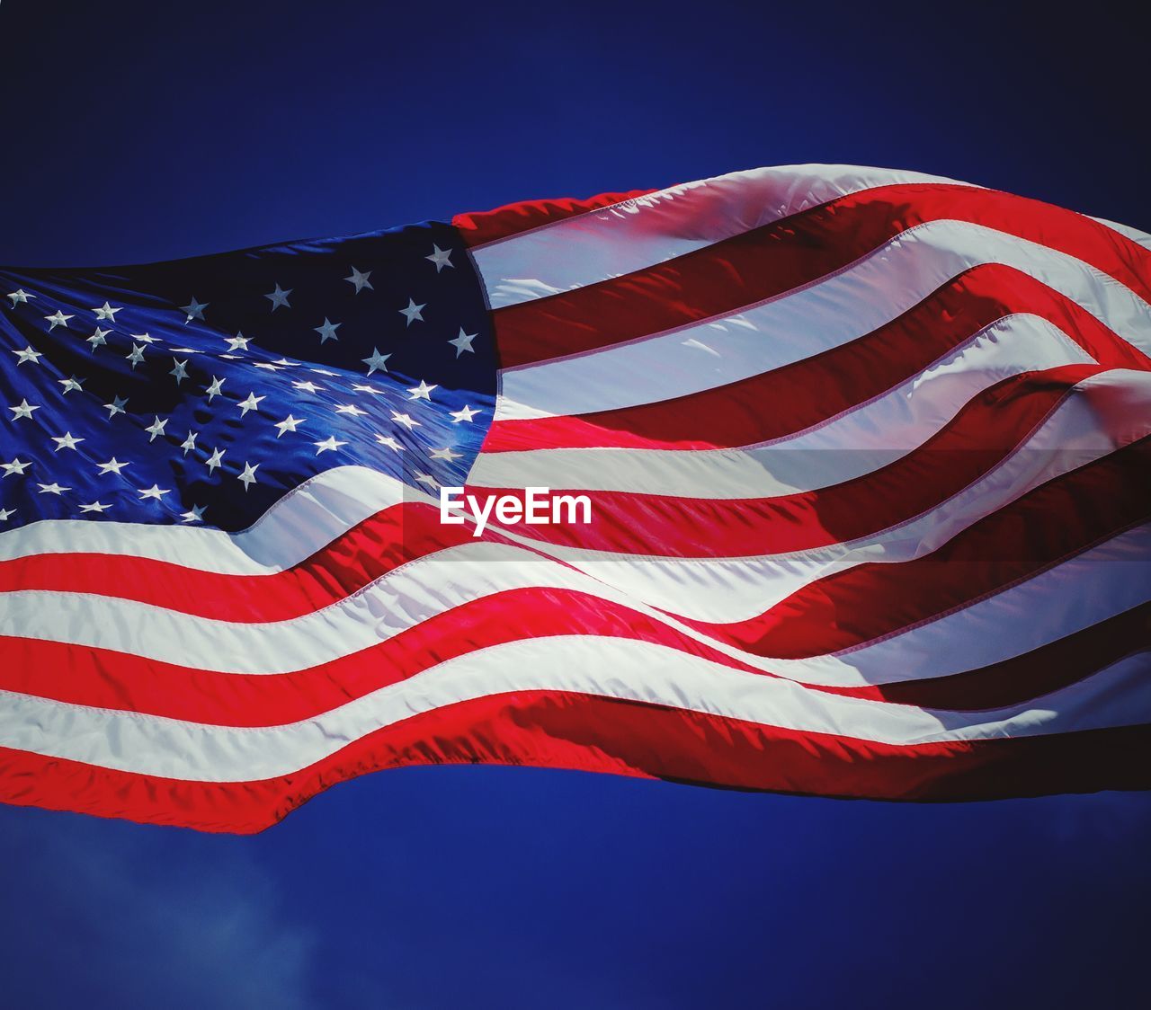 Low angle view of american flag waving against blue sky