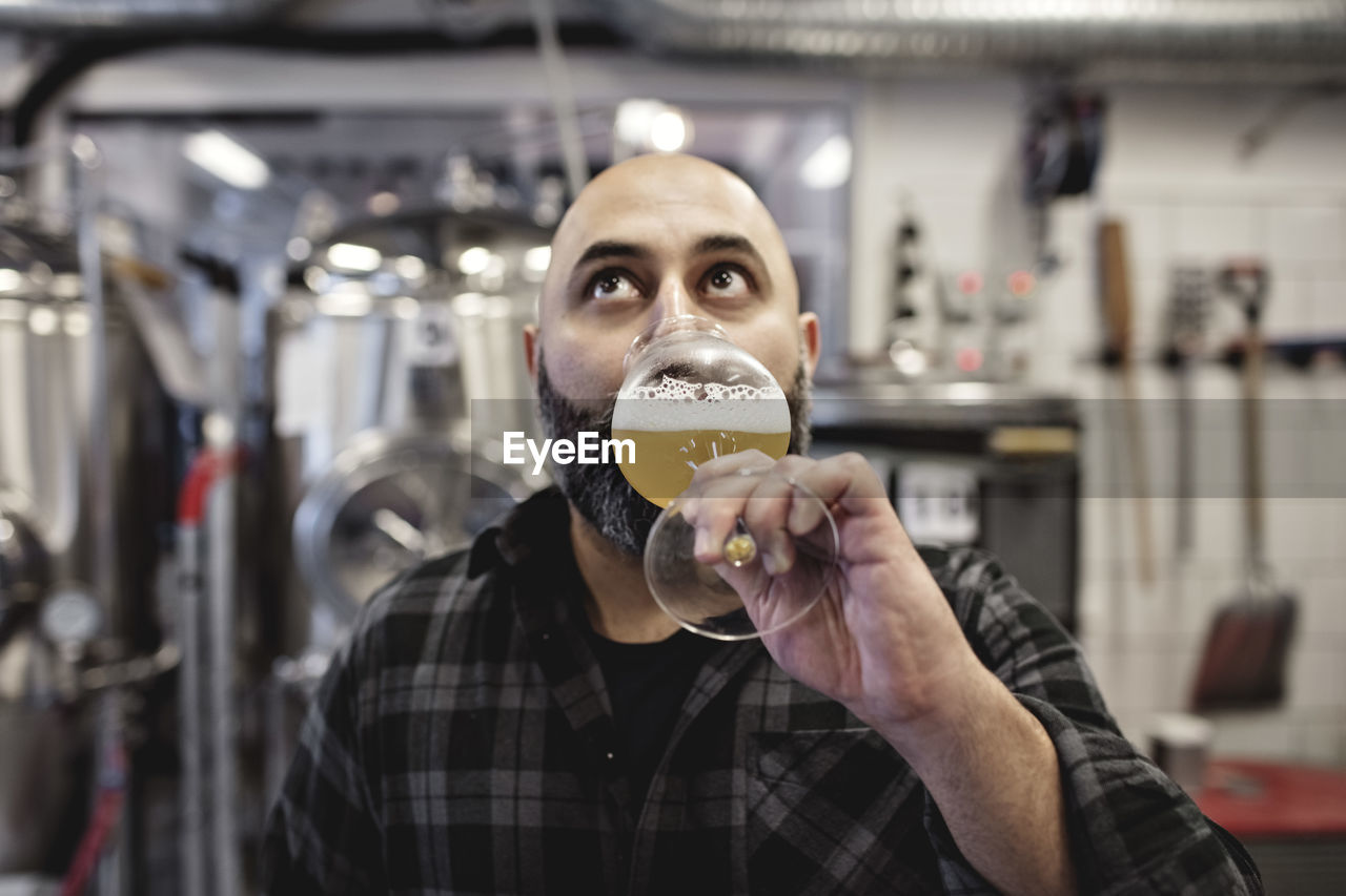 Male worker tasting craft beer while standing at factory