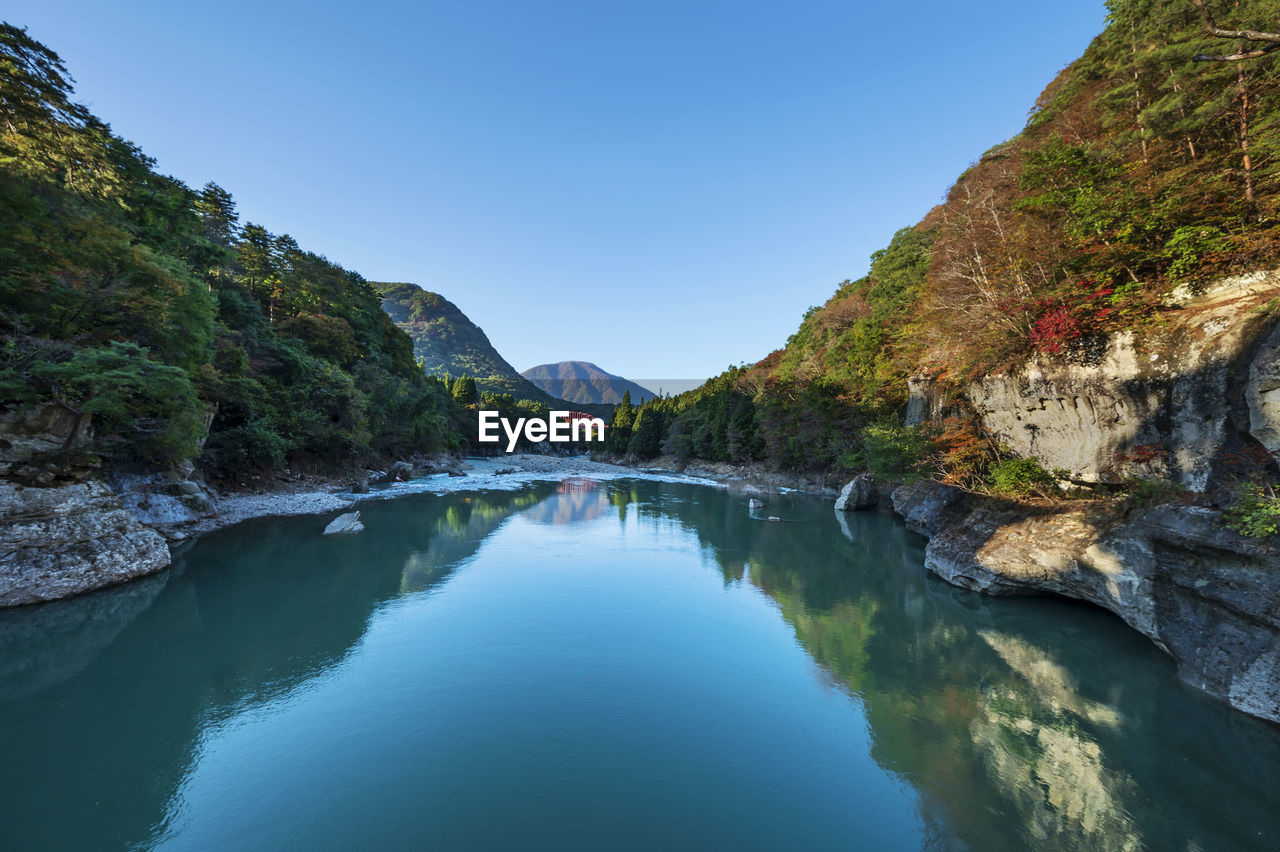 Scenic view of river amidst mountains against clear blue sky