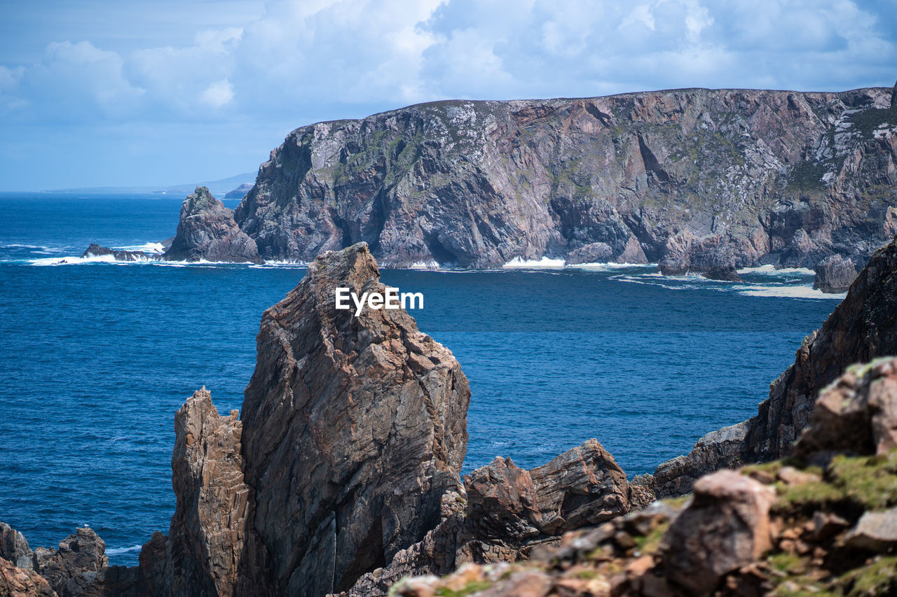 Scenic view of rocks by sea against sky